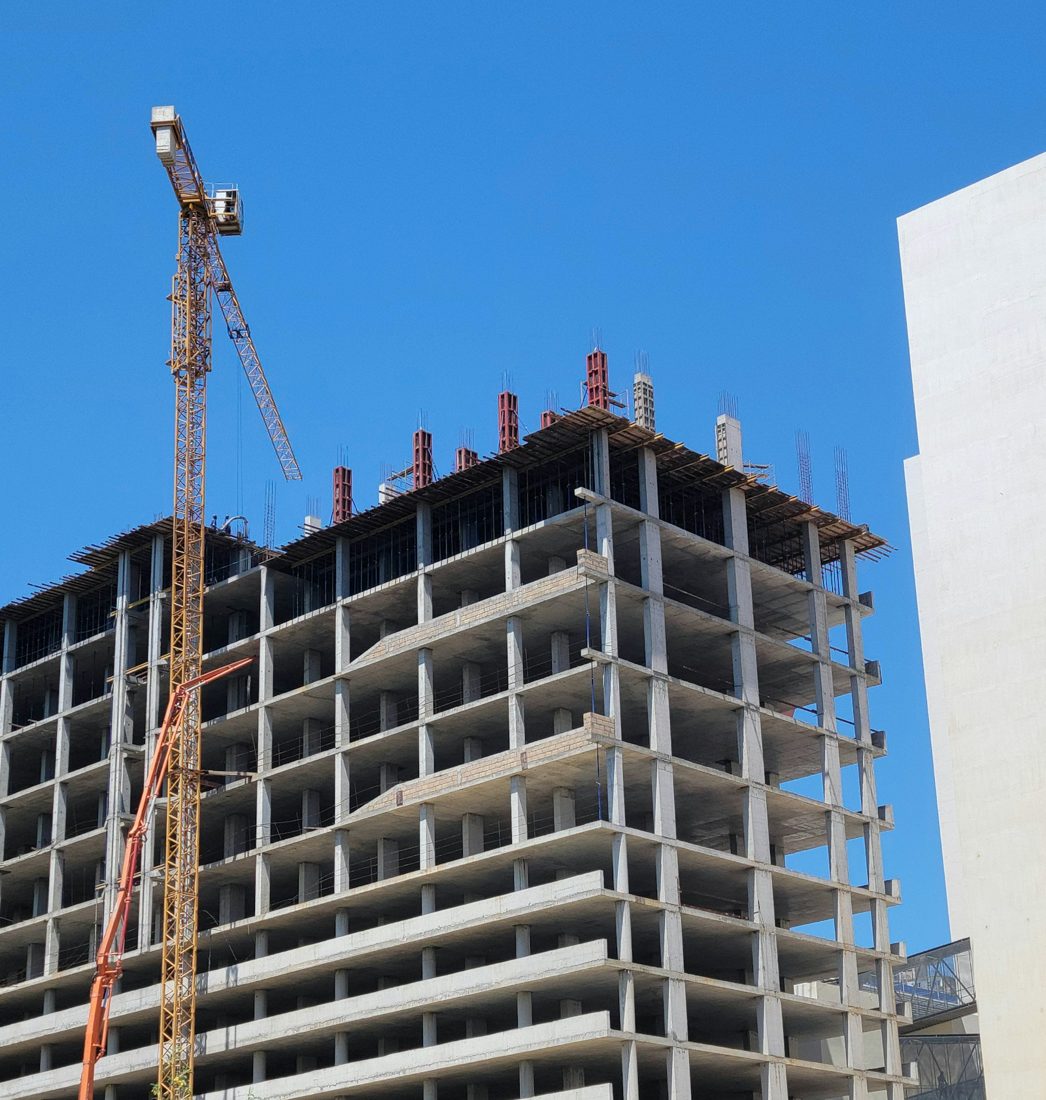 A concrete-frame building under construction beside a tower crane