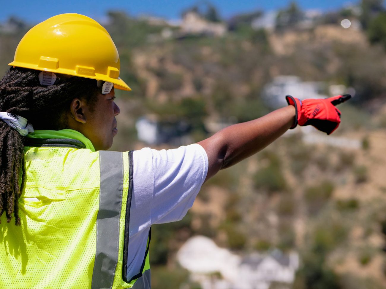An engineer in a yellow hard hat and hi-vis vest pointing across a construction site